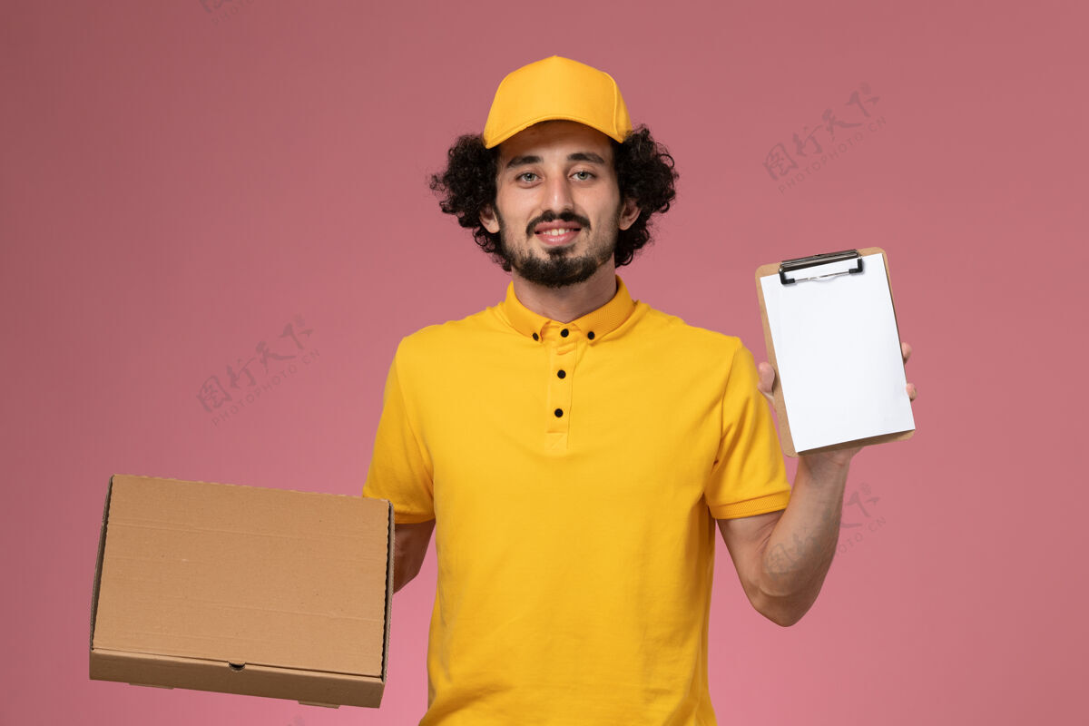 黄色正面图穿着黄色制服的男快递员拿着食品快递箱和笔记本放在粉红色的墙上粉色成人服务